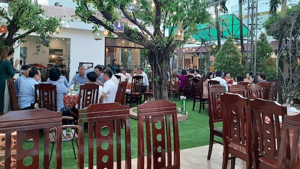 Un espace de restauration en plein air, avec des tables et des chaises en bois, entouré de verdure et d’arbres.