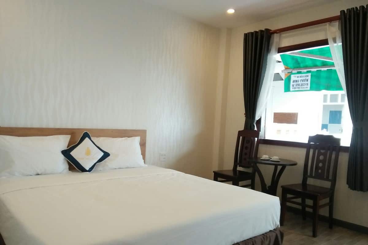 Ein Hotelzimmer mit einem Bett, einem kleinen Tisch, zwei Stühlen und einem Fenster mit Vorhängen.