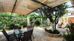 Un patio al aire libre con una mesa y sillas, rodeado de plantas en macetas y un piso de piedra.