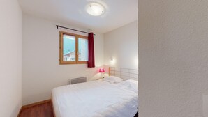 Un dormitorio con cama, ventana con cortinas, lámpara de noche y radiador.