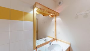 Un baño con tocador de madera, lavamanos blanco y espejo.