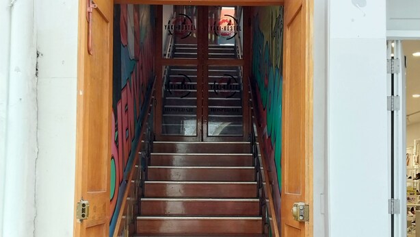 Un escalier en bois mène à l’entrée d’une auberge de jeunesse, où un panneau indique « YAKI-HOSTEL ».