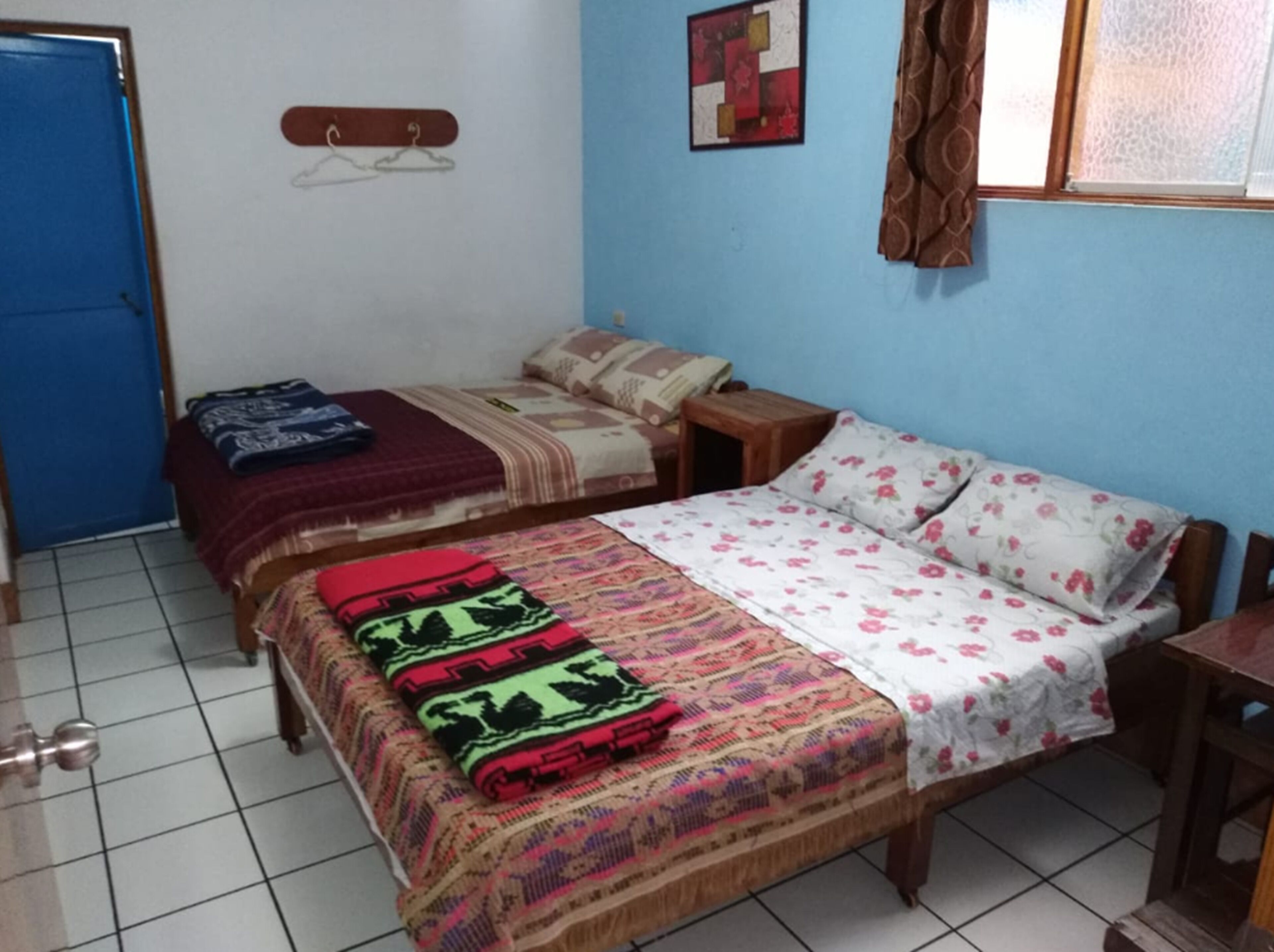 Una camera da letto con due letti, un armadio in legno, un tavolino e una finestra con tende.