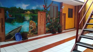 Un couloir orné d’une fresque représentant une scène de jungle, une porte en bois portant l’inscription « El Amazonas », et un escalier.