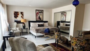 A hotel room with a bed, two armchairs, a desk, a mirror, and artwork on the walls. - Greenway Manor (Bisbee)