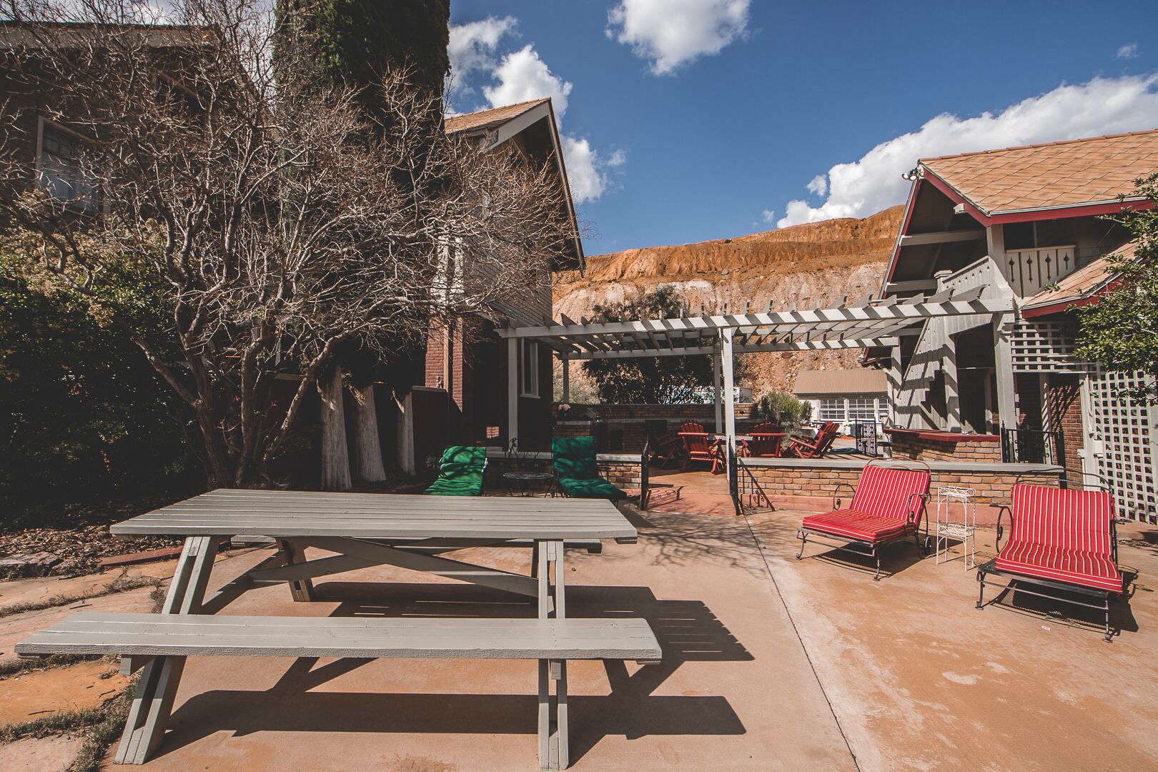 Un área de patio al aire libre con una mesa de picnic, sillas rojas a rayas y una estructura de pérgola.
