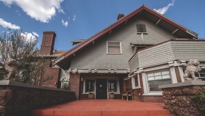 A two-story house with a red roof, brick exterior, and stone lion statues at the entrance. - Greenway Manor (Bisbee)