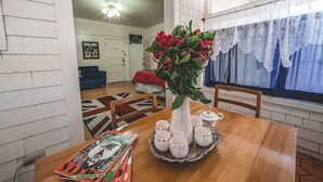 A dining area with a wooden table, a vase of red flowers, and a tray with teacups. - Greenway Manor (Bisbee)