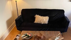 A living room with a black sofa, a wooden coffee table, a cowhide rug, and a lamp. - Greenway Manor (Bisbee)