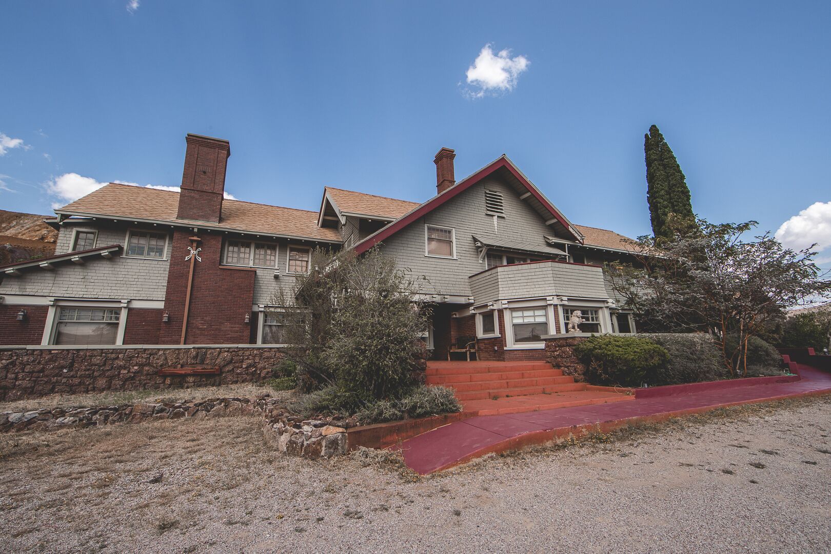 Uma casa de dois andares com varanda frontal vermelha, chaminés de tijolo e alicerce de pedra.