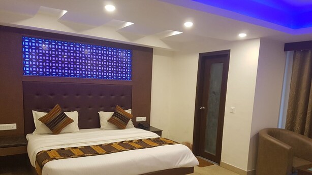 Een moderne hotelkamer met een groot bed, een hoofdbord met een geometrisch lichtpaneel, een bruine fauteuil en een deur met een ruit.