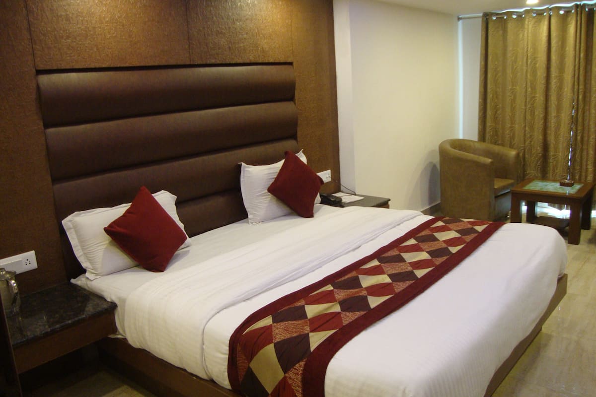 Quarto de hotel com uma cama grande, cabeceira de madeira, uma cadeira e uma mesinha de cabeceira.