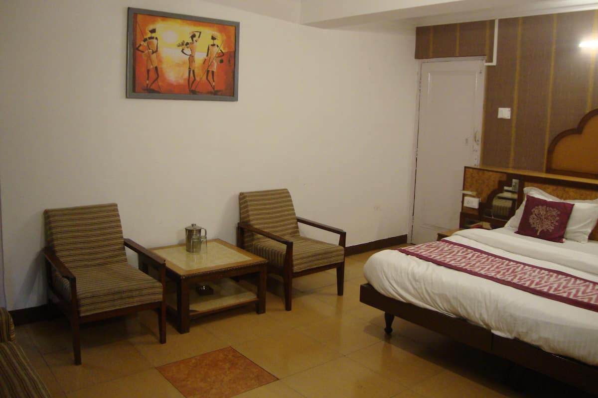 Quarto de hotel com uma cama, duas poltronas, uma mesinha e um quadro na parede.