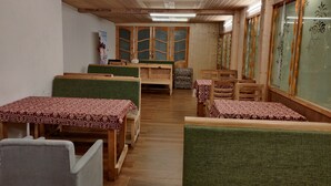 Een kamer met houten balken in het plafond, groene beklede stoelen en tafels met tafelkleden met dessin.