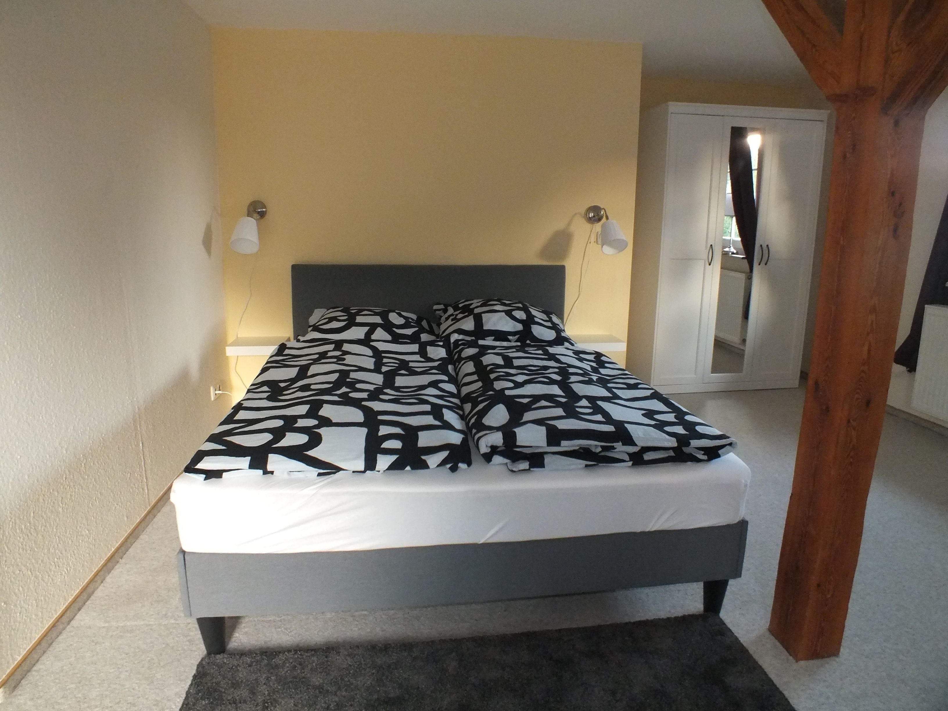 Ein Bett mit einem gemusterten Überwurf, einer Nachttischlampe und einer Tür im Hintergrund.