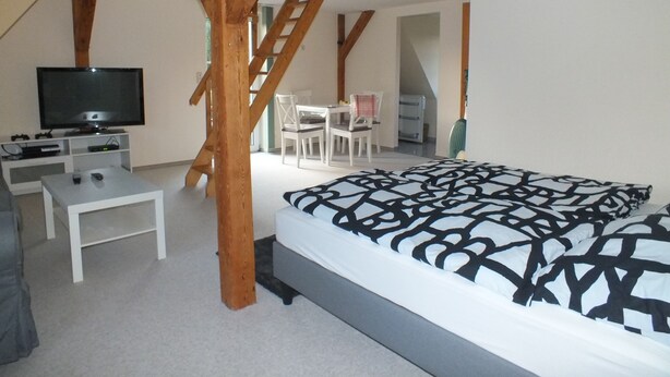 Un dormitorio con cama, televisión, escritorio y escalera.