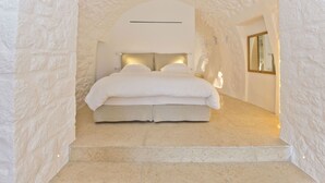 A bedroom with a stone wall, a bed with white bedding, and a mirror on the wall. - Pirgos Mavromichali (East Mani)