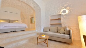 A cozy room with a bed, a sofa, and a small table with fruit. There is a stone wall and a circular light fixture. - Pirgos Mavromichali (East Mani)