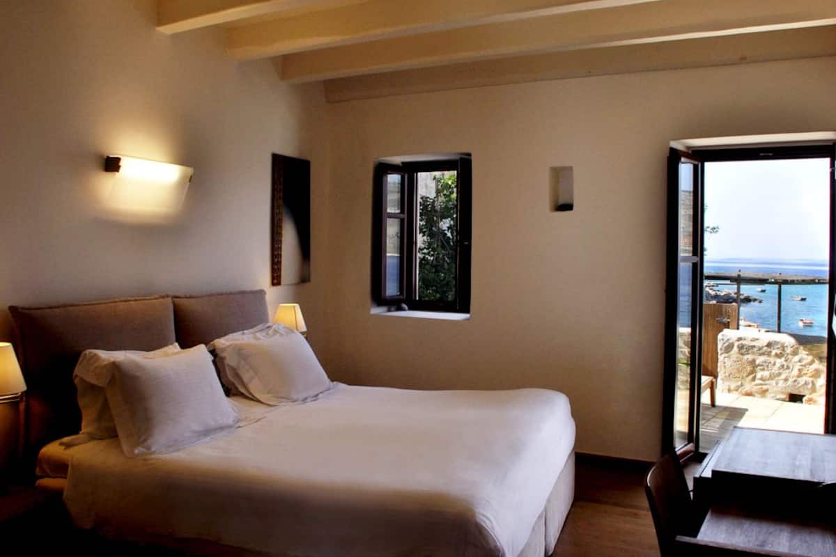 Un dormitorio con cama, lámparas de noche, una ventana y vista al mar.