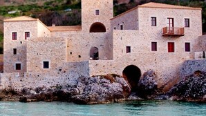 A coastal stone building with multiple windows and a tower, situated by the sea. - Pirgos Mavromichali (East Mani)