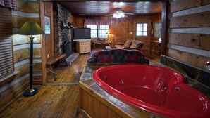Een houten interieur met een rode hottub, houten vloeren, een stenen openhaard, een televisie en een plafondventilator.