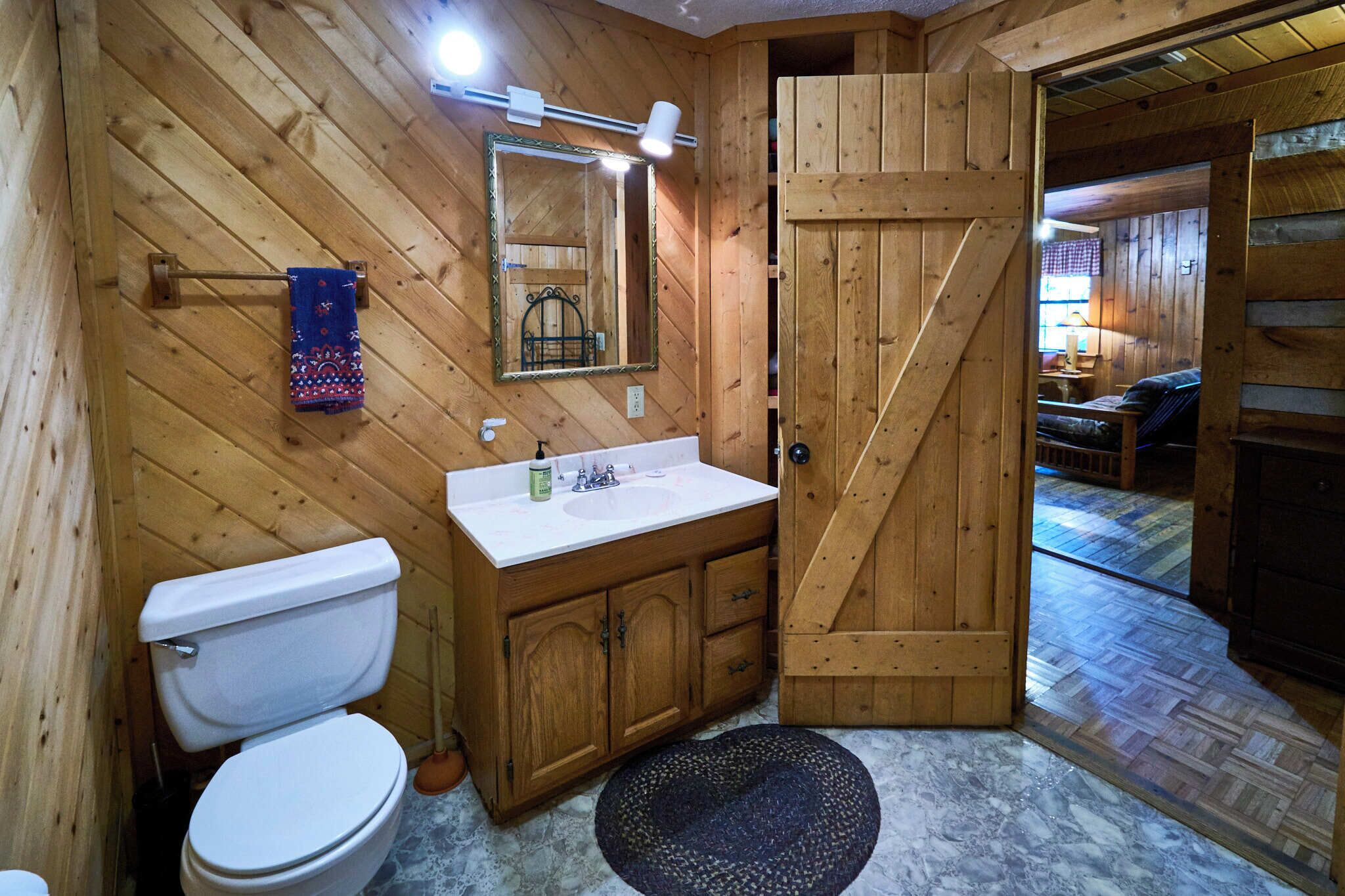 A wooden bathroom with a toilet, sink, and mirror.