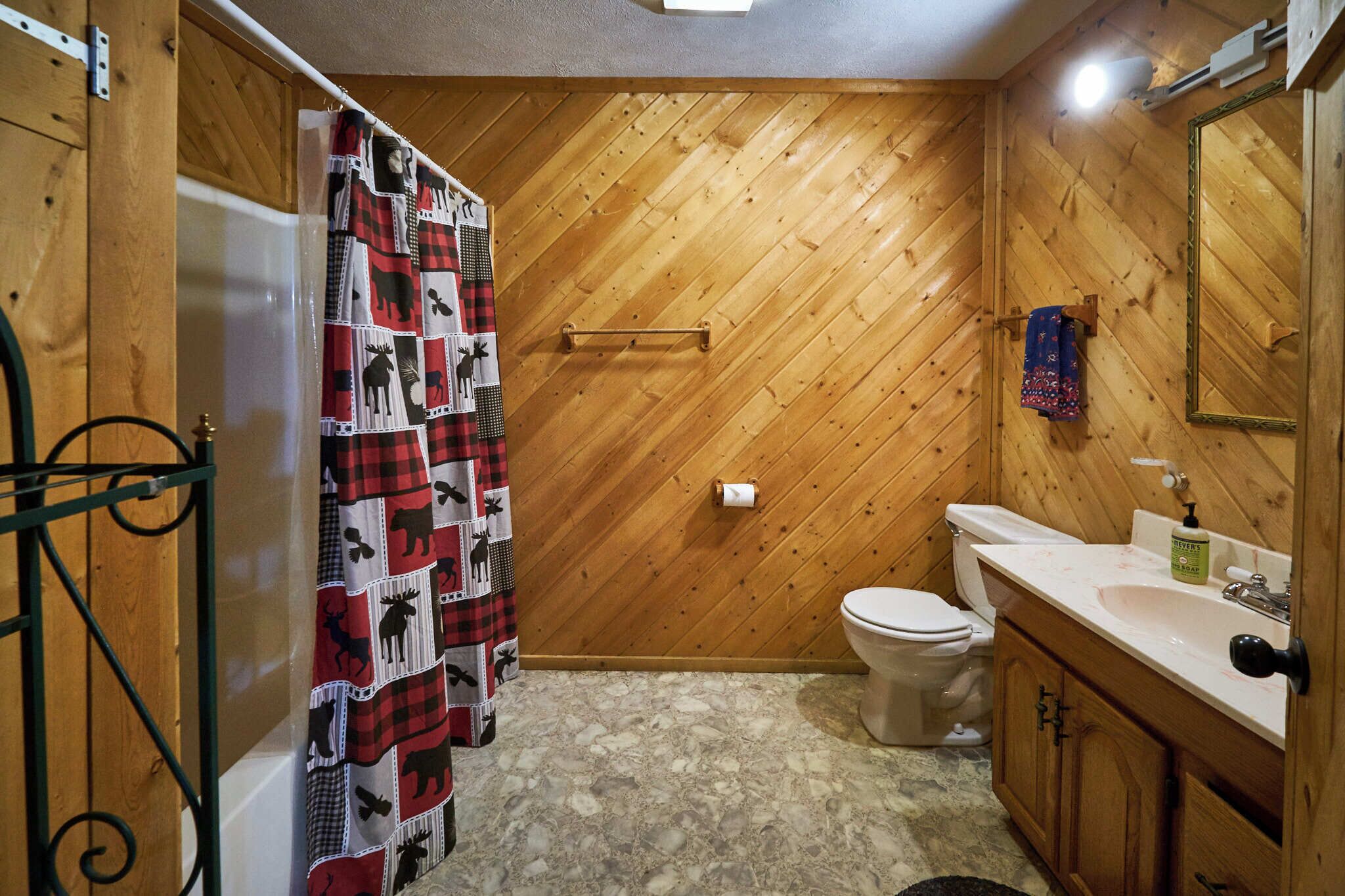 A bathroom with a wooden herringbone wall, a white toilet, a sink with a soap dispenser, and a shower curtain with animal prints.