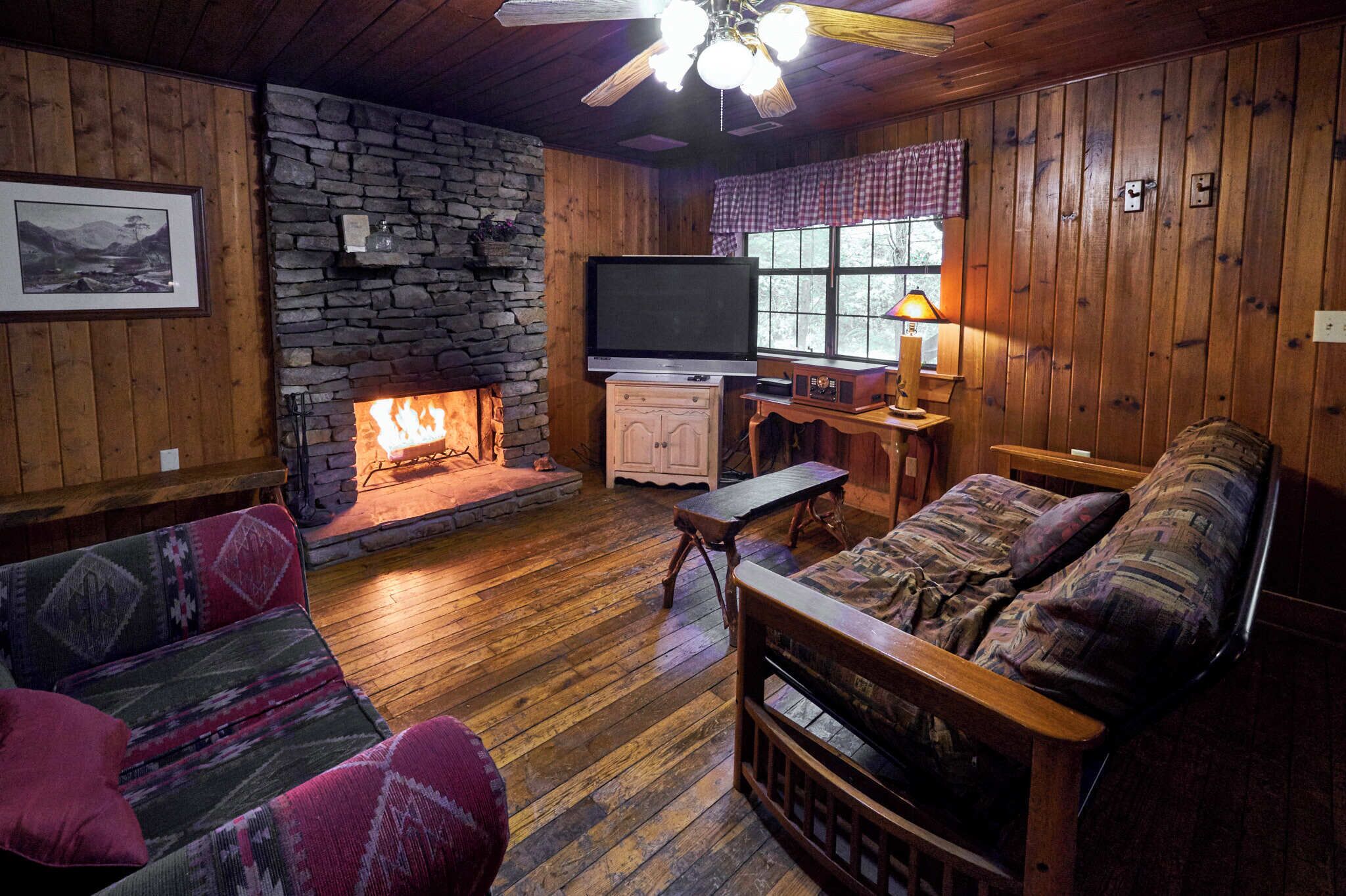 A cozy living room with a stone fireplace, wooden furniture, and a flat-screen TV.