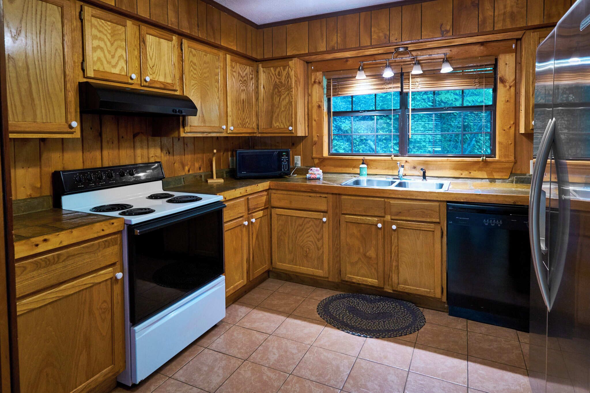 A kitchen with wooden cabinets, a stove, a microwave, a sink, and a refrigerator.