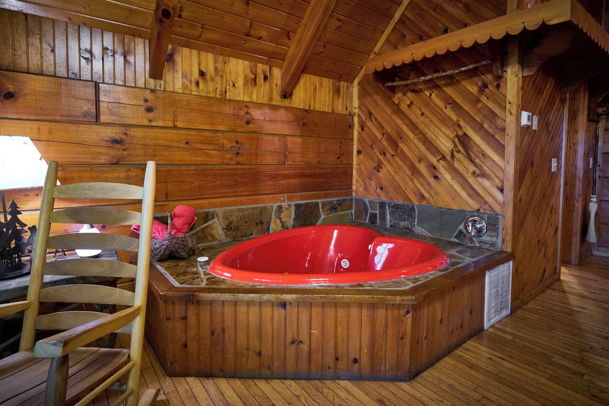 A wooden cabin interior with a wooden chair, a red hot tub, and a stone wall.
