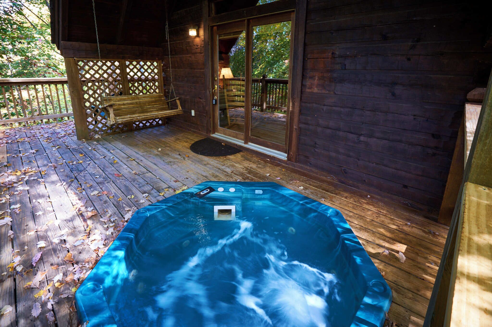 A wooden deck with a hot tub, wooden benches, and a glass door leading to a deck area.