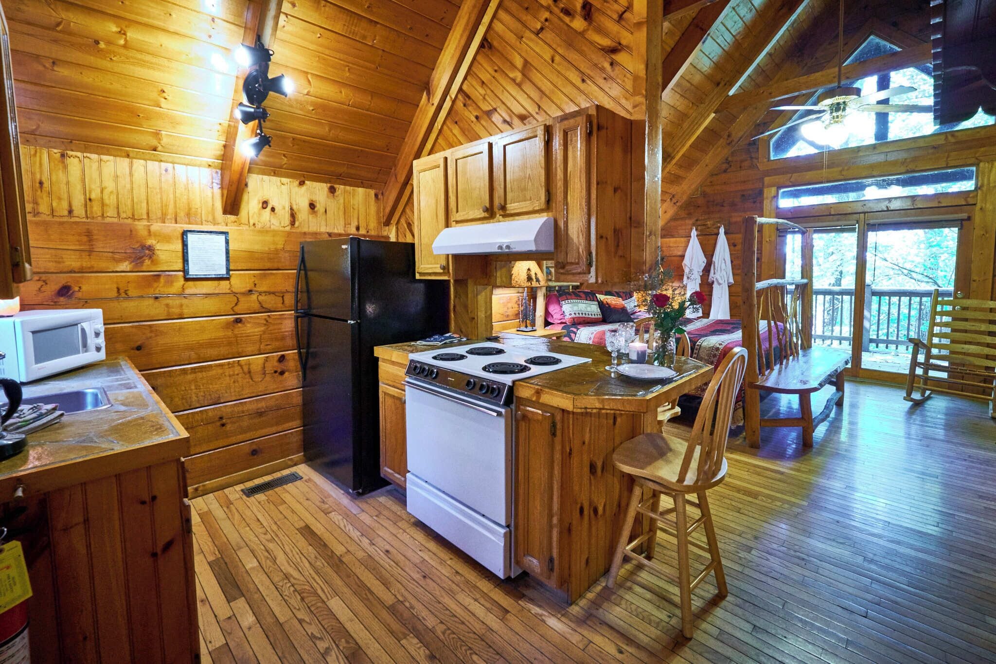 A wooden cabin interior with a kitchen featuring a stove, refrigerator, and wooden cabinets.
