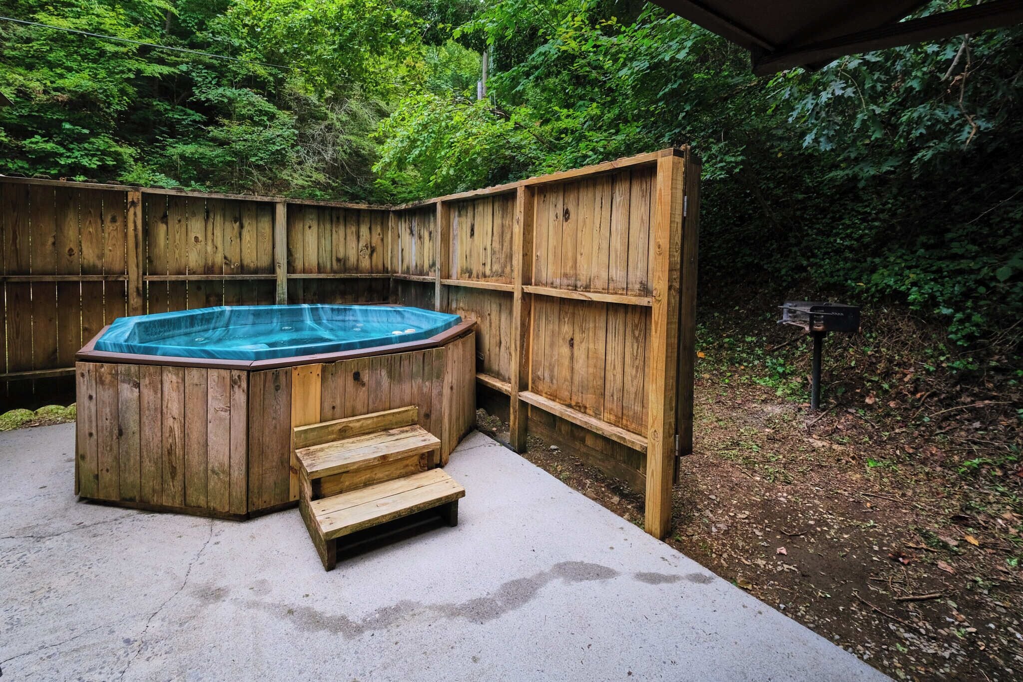 A wooden hot tub with steps leading up to it, surrounded by a wooden fence and lush greenery.