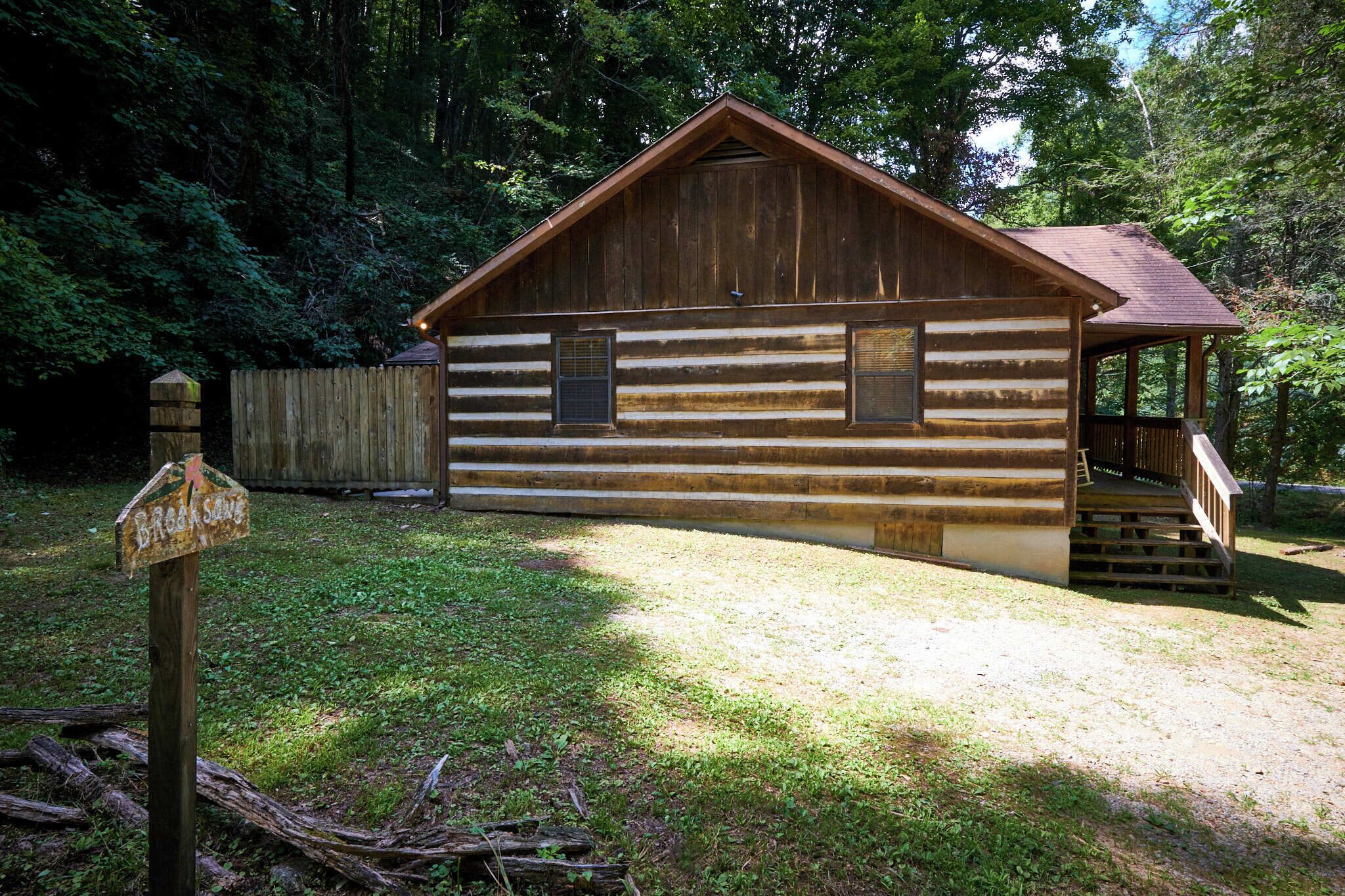 A rustic log cabin with a porch and a wooden fence in the background.