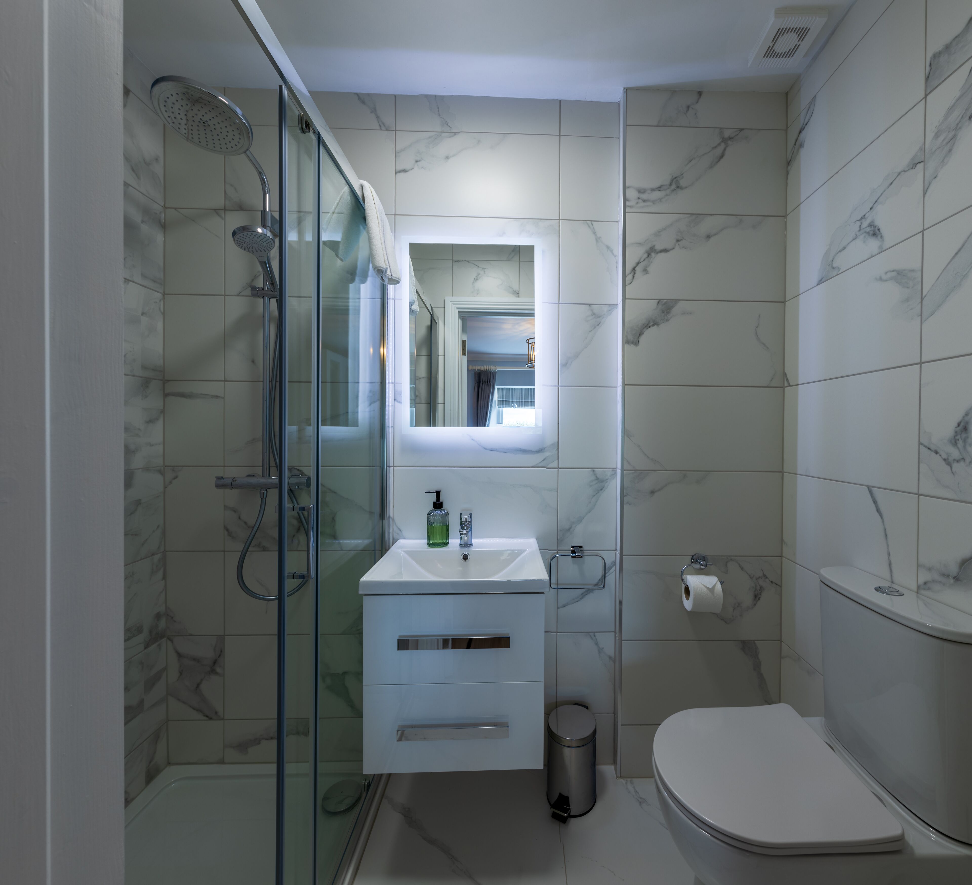 Un baño moderno con ducha de vidrio, un lavamanos blanco con espejo arriba y un inodoro.