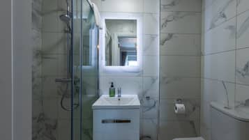 Un baño moderno con ducha de vidrio, un lavamanos blanco con espejo arriba y un inodoro.