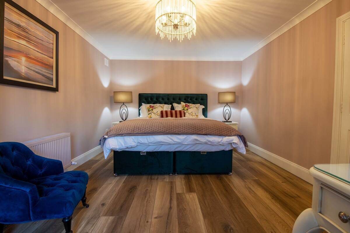 Ett sovrum med en stor säng, två sänglampor, en kristallkrona, en blå stol och ett element.