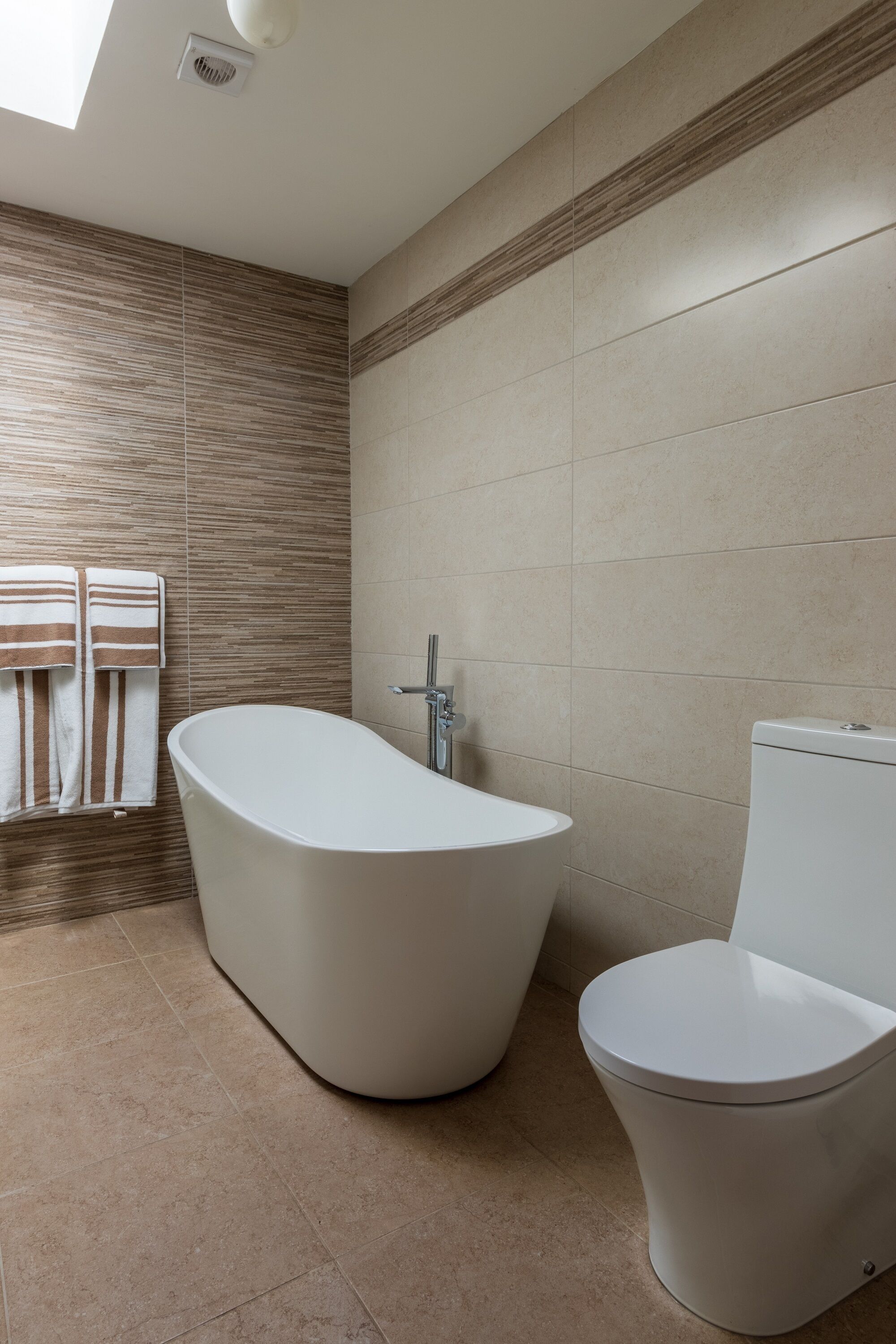 A modern bathroom with a freestanding bathtub, a toilet, and a towel rack with two towels.