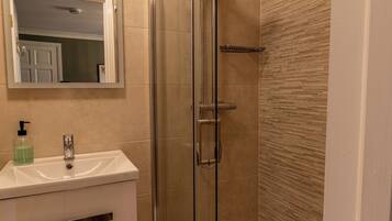 Un baño moderno con ducha de vidrio, un lavamanos blanco con dispensador de jabón y un espejo sobre el lavamanos.