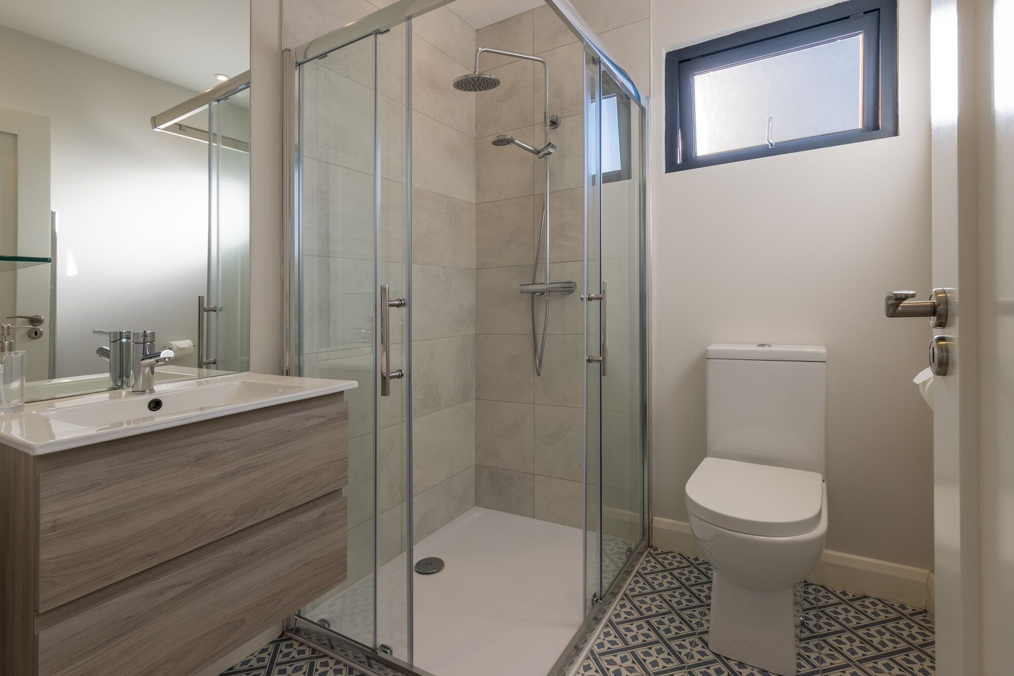 Un baño moderno con ducha envuelta en vidrio, inodoro blanco y tocador con espejo.