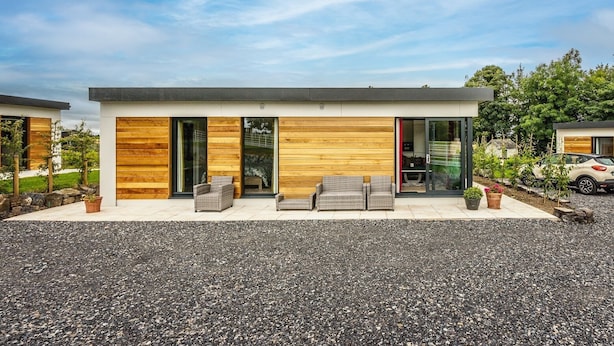 Una casa moderna con camino de grava, paredes exteriores de madera y un patio con mobiliario de exterior.