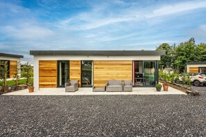 Una casa moderna con camino de grava, paredes exteriores de madera y un patio con mobiliario de exterior.