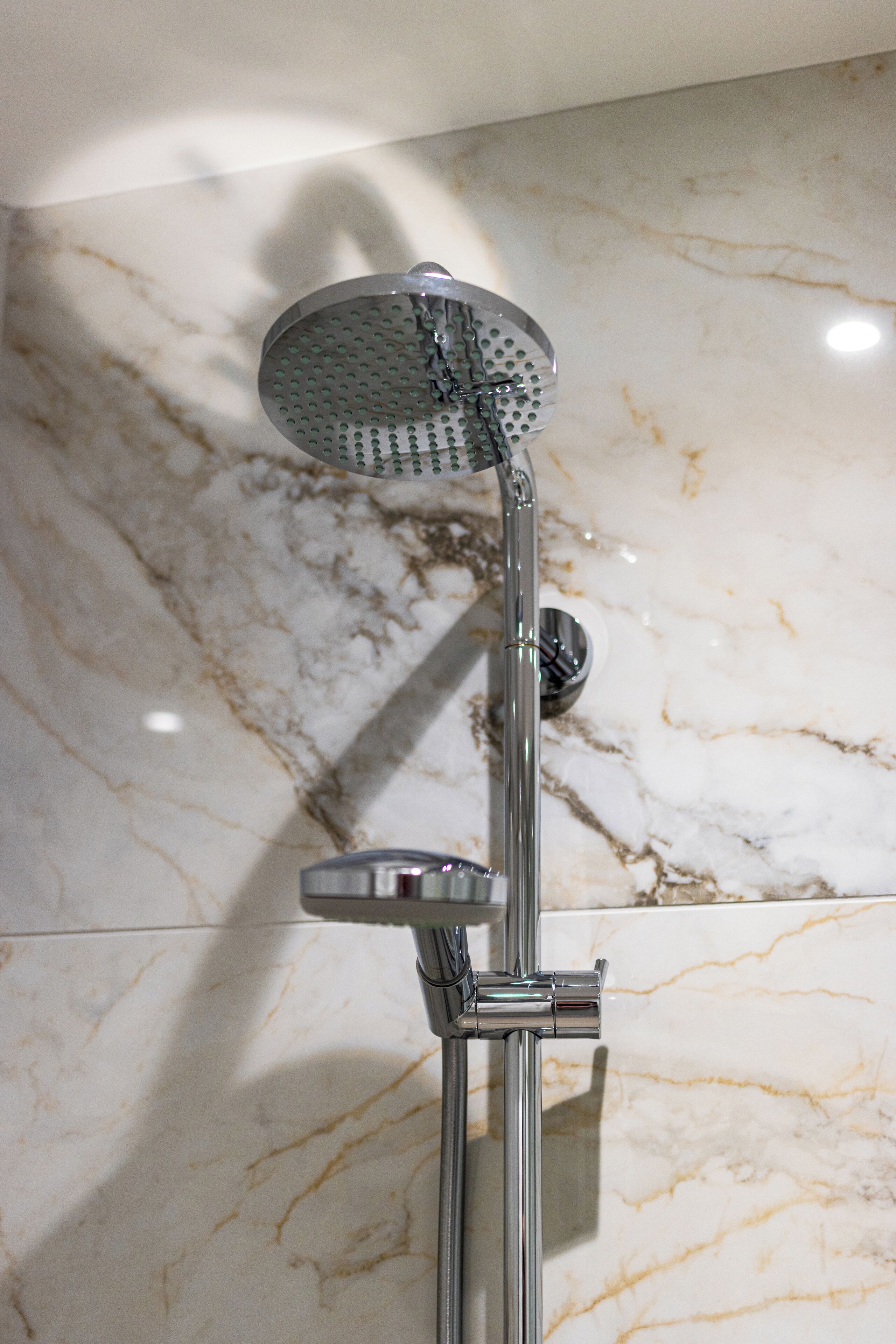 A showerhead with a handheld attachment, mounted on a chrome fixture against a marble wall.