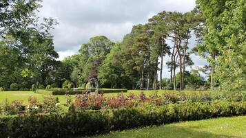A well-maintained garden with manicured lawns, a variety of shrubs, and tall trees.