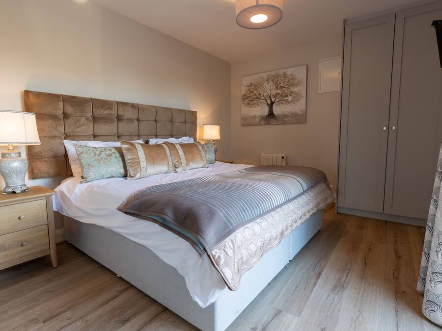 A bedroom with a large bed, bedside tables, a wardrobe, and a painting of a tree.