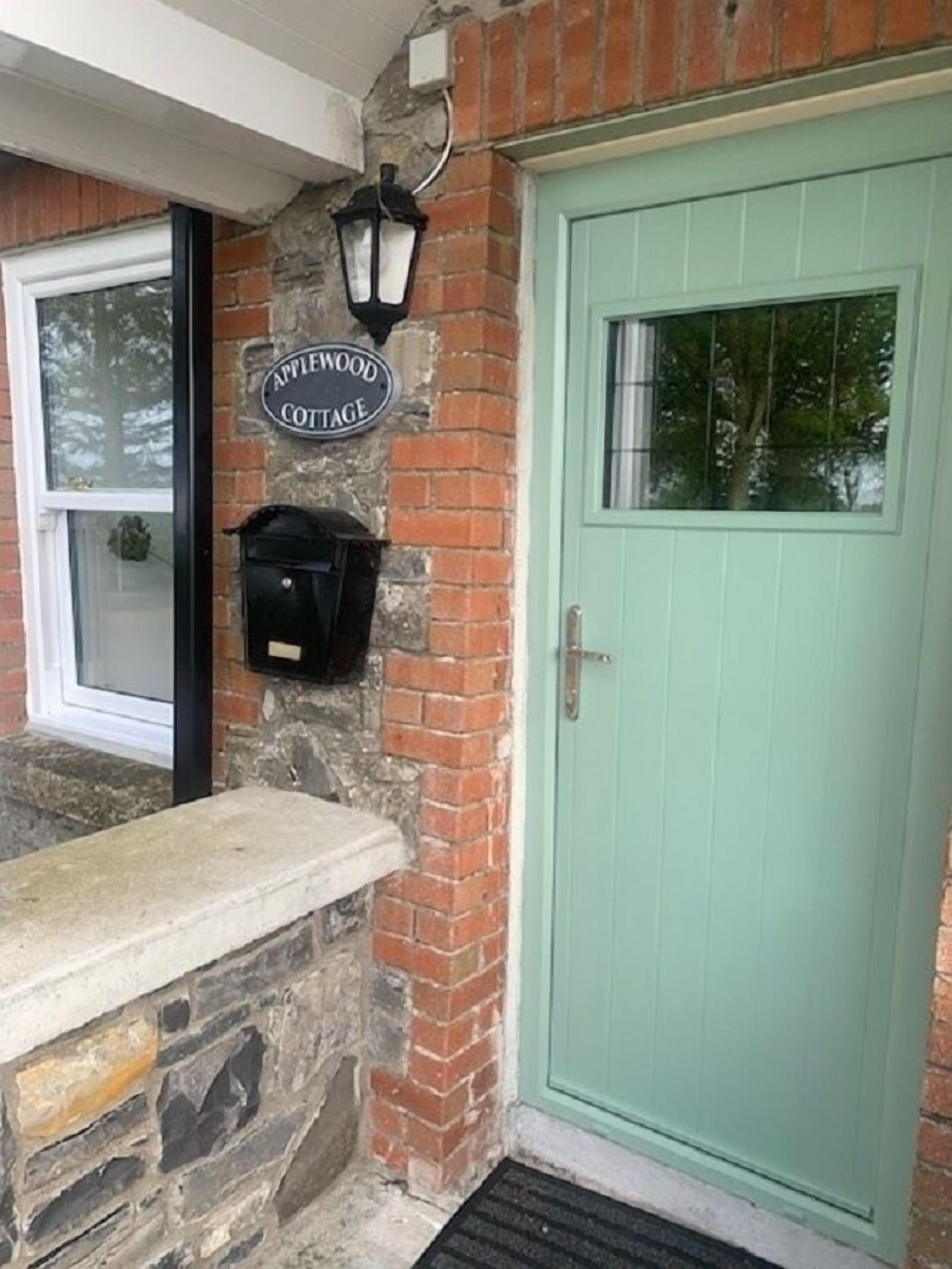Entrada de um chalé com muro de pedra, porta verde e placa com a inscrição 'Applewood Cottage'.