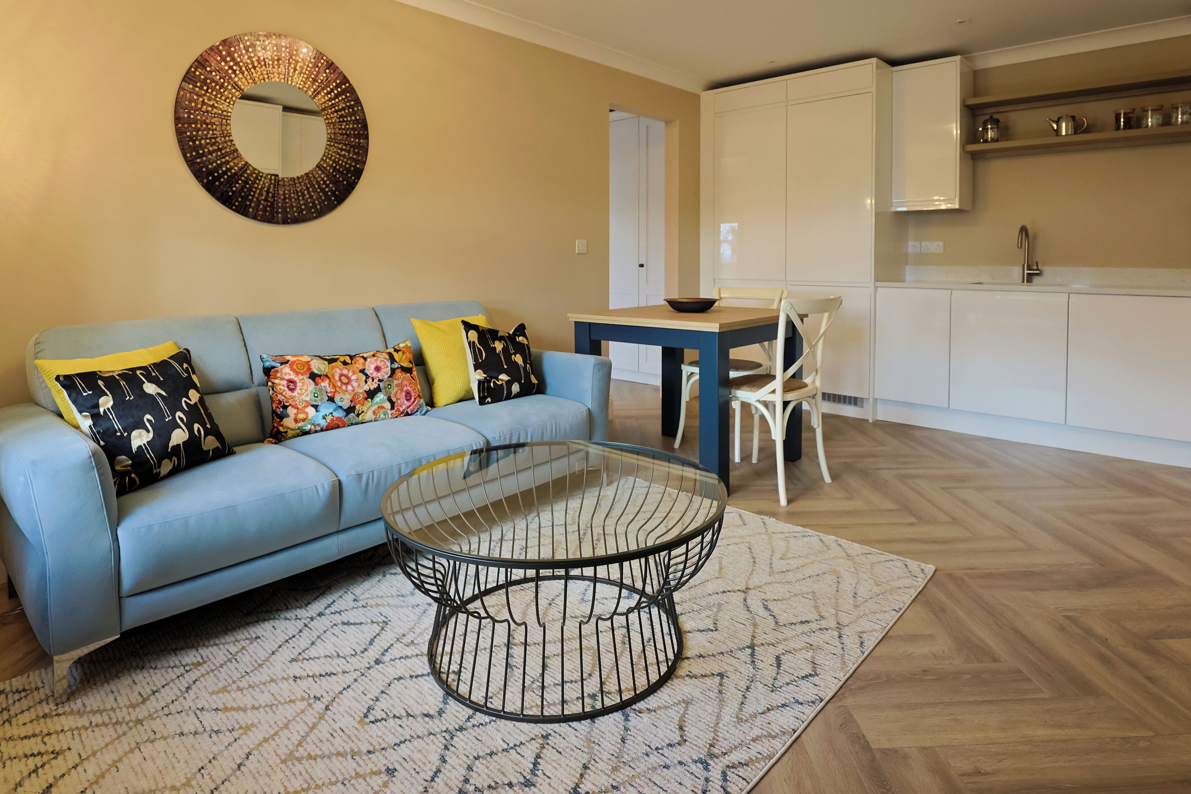 A living room with a blue sofa, a glass coffee table, and a dining table with chairs.