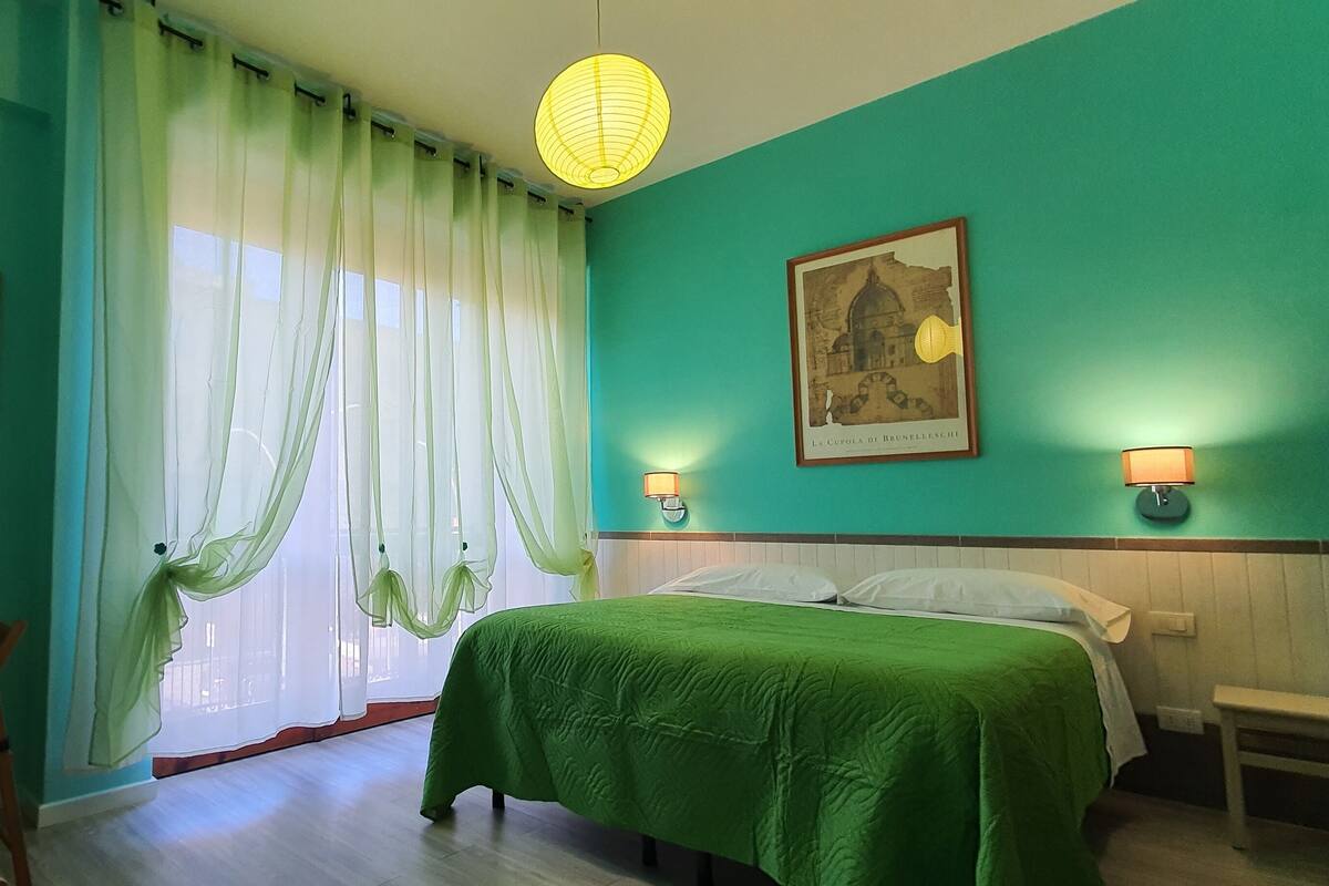 Ein Zimmer mit einem Bett, einem Sessel, einem Tisch und einer Heizung. An den Wänden befinden sich zwei Wandleuchten und zwei gerahmte Bilder.