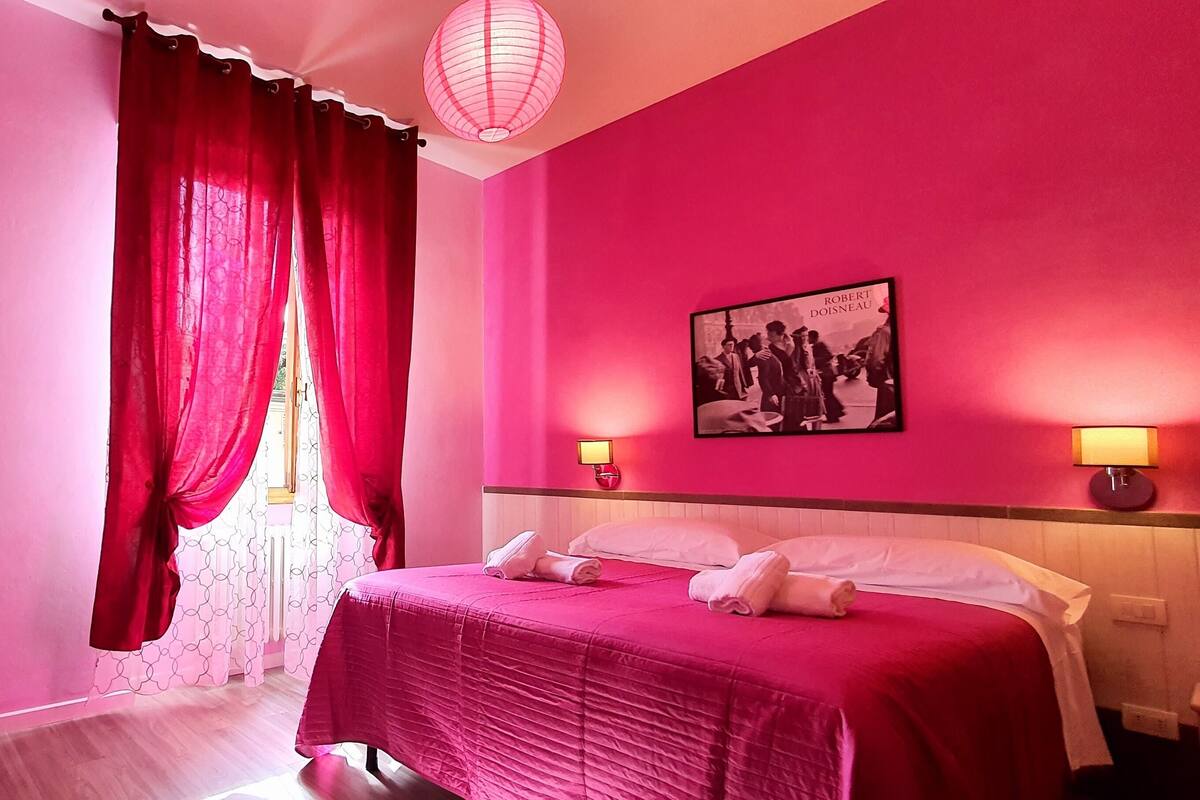 Ein Hotelzimmer in Rosa mit einem Bett, einem Schreibtisch und einem Stuhl.