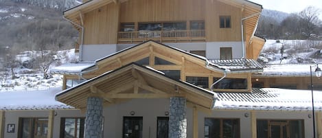 Un bâtiment en bois à deux étages, avec une base en pierre, un balcon à l’étage supérieur et un toit recouvert de neige.